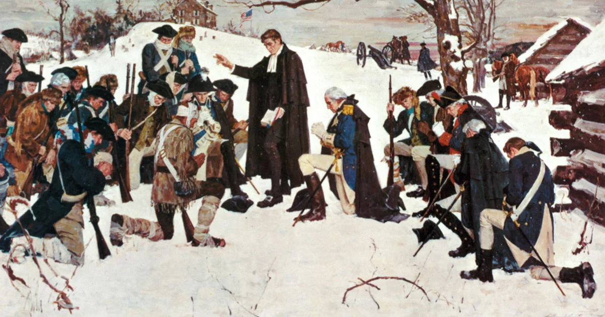 A group of men in historic military attire gather around a standing man in a coat, gesturing. The scene is set outdoors in a snowy landscape, with a log cabin and horses in the background.