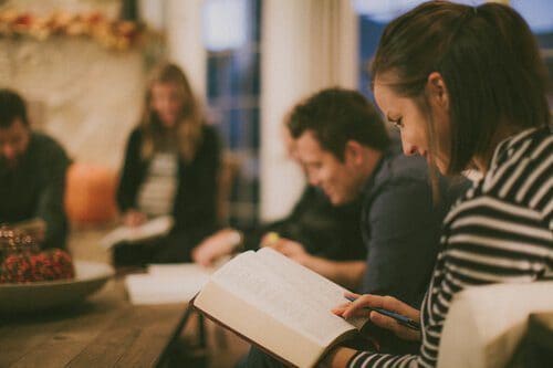 A group of people sits together indoors, reading and discussing books around a table.