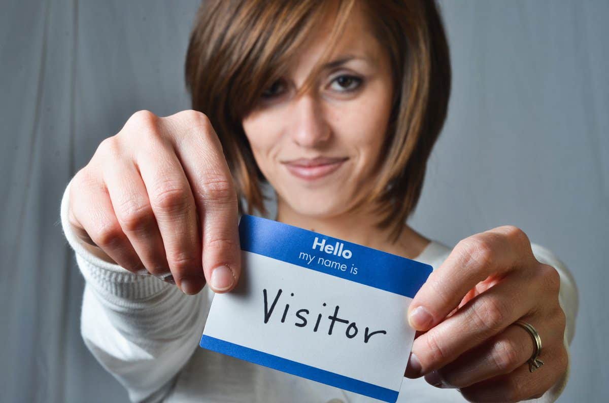 A woman holding a "Hello, my name is Visitor" name tag, smiling at the camera.